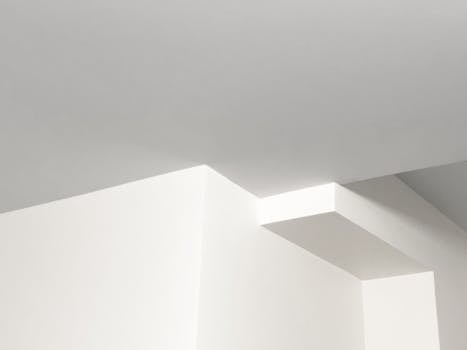 A minimalist design featuring a white ceiling with geometric structures creating soft shadows.