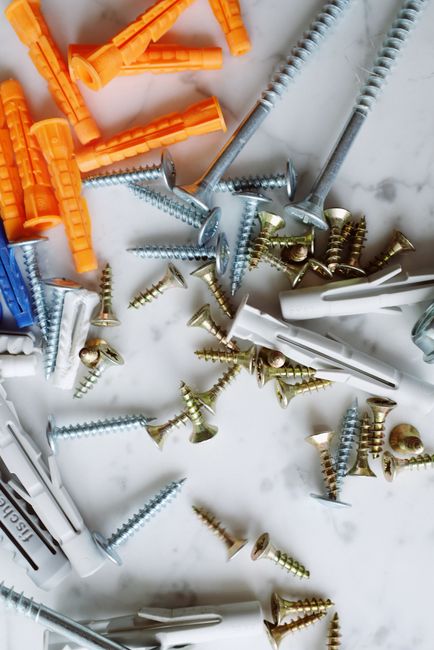 Set of various multicolored plastic dowels with metal screws of different sizes placed on white marble table in modern workshop