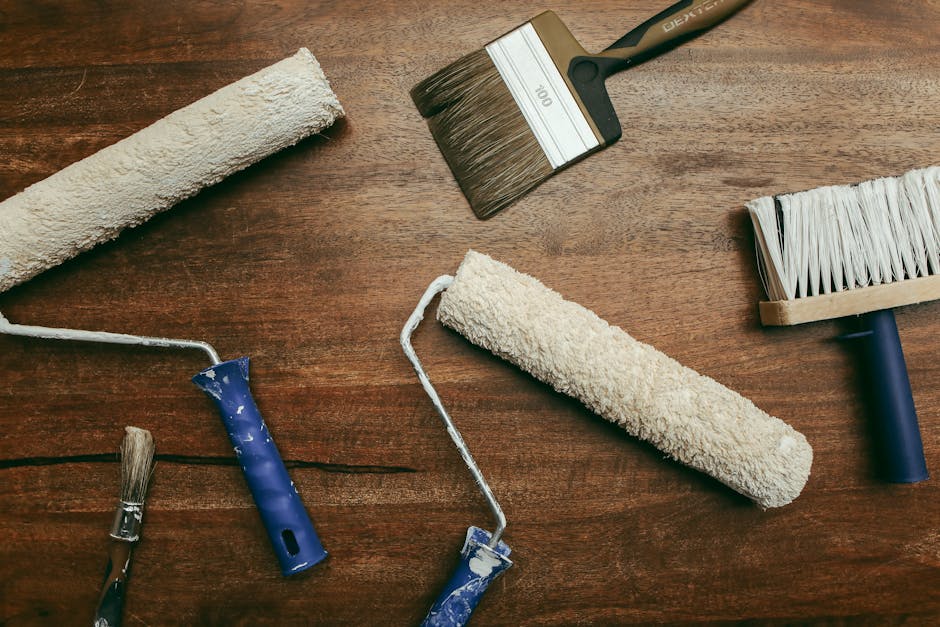 Top view of various painting tools including rollers and brushes laid out on a wooden surface.