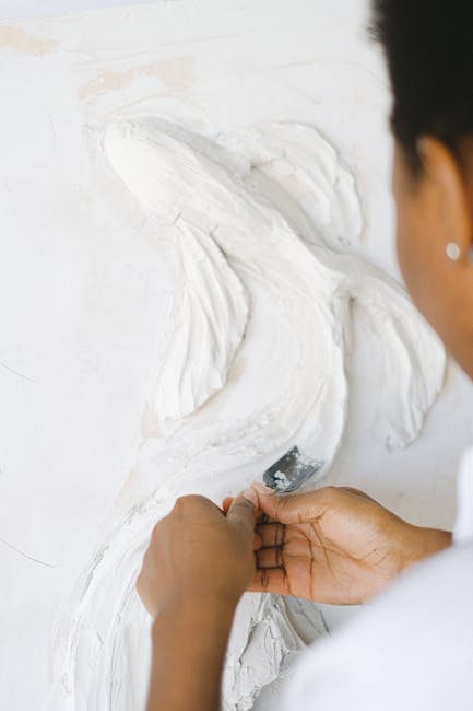 Close-up of a woman artist sculpting a fish design in plaster on a vertical surface.